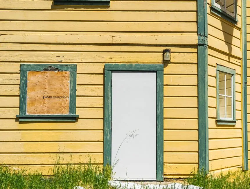 Close-up of a yellow wooden facade with a closed door and boarded window.